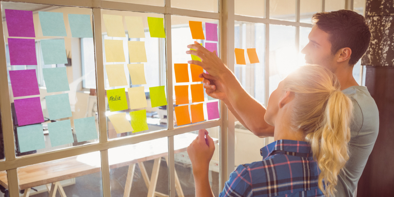 Two young people looking at post-it notes on a board