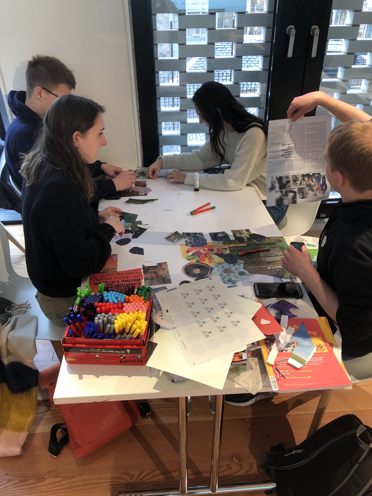 four young people sit around a table while making posters