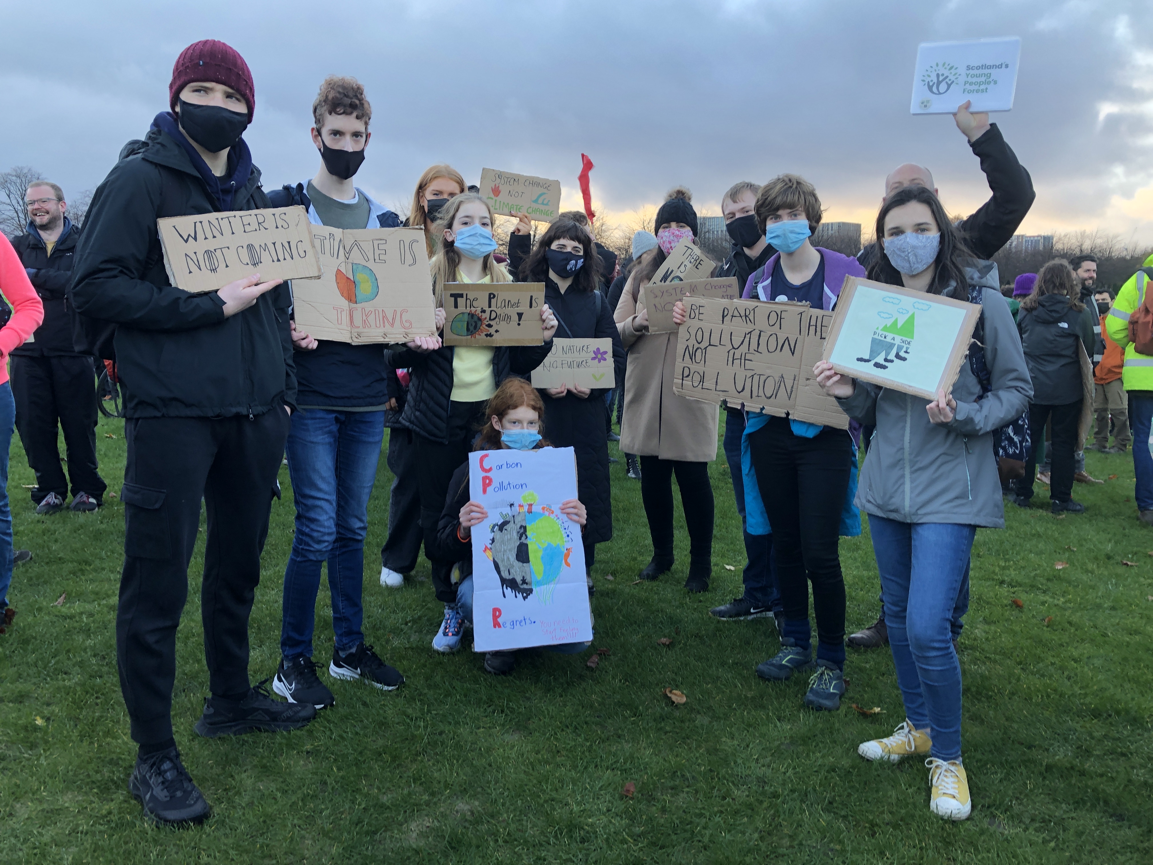 a group of young people stand in together on grass, each holding placards related to climate change