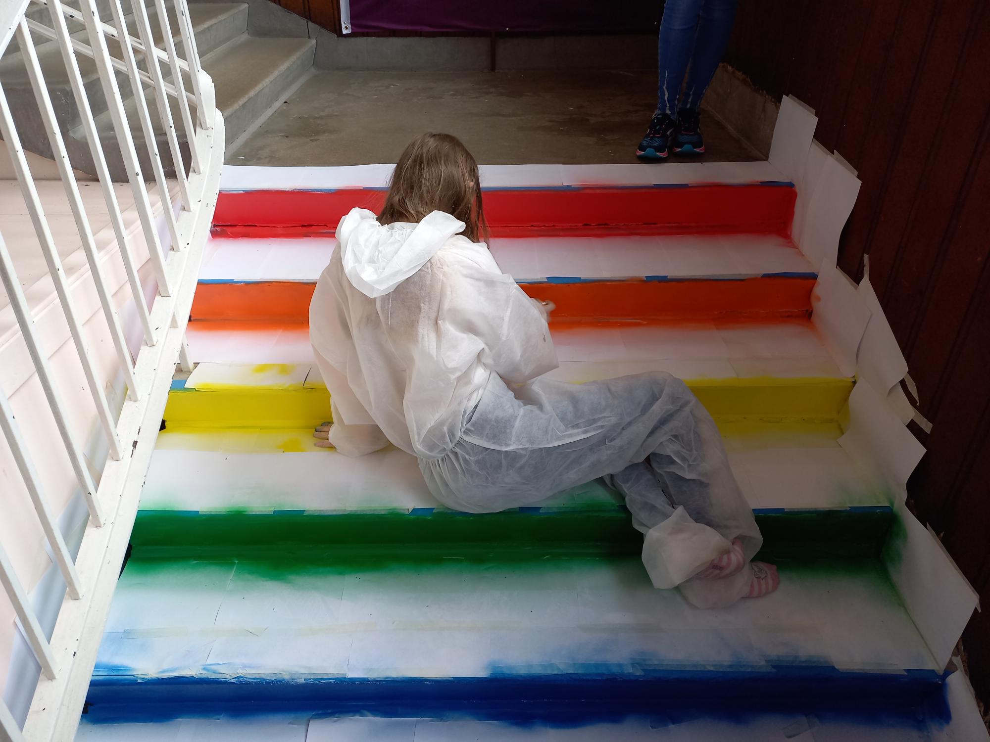 Zoe at work painting the stairs with the colours of the pride flag